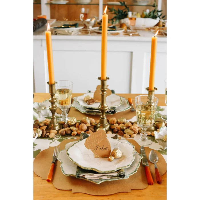 Create a festive Thanksgiving tablescape with Hester & Cook’s Acorn Place Card - Pack of 12, gold candlesticks with orange candles, scalloped plates, white wine glasses, and autumnal accents—ideal for fall celebrations.