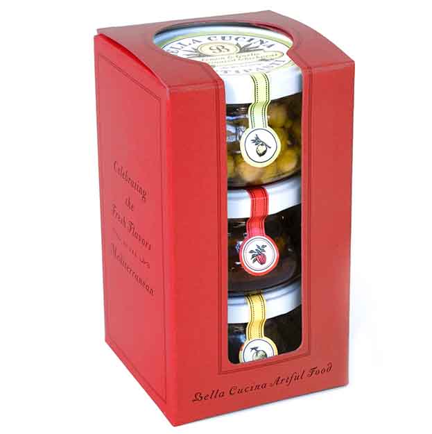 Bella Cucina’s Antipasti Gift Box features three stacked condiment jars with assorted labels, showcased in a red box with a clear front and “Bella Cucina Artful Food”—ideal for cheese boards or charcuterie.