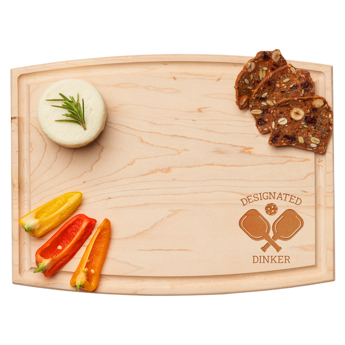 The Maple Arched Artisan Maple Board | Designated Dinker | 12 x 9" features two crossed pickleball paddles and comes displayed with a cheese wheel, rosemary, colorful pepper slices, and three seed-and-nut crispbreads.