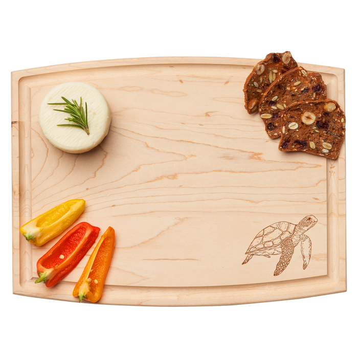 The Maple Arched Artisan Maple Board | Turtle | 12 x 9" features a carved turtle design, shown serving bell pepper slices, rosemary-topped round cheese, and nut and fruit crisps.