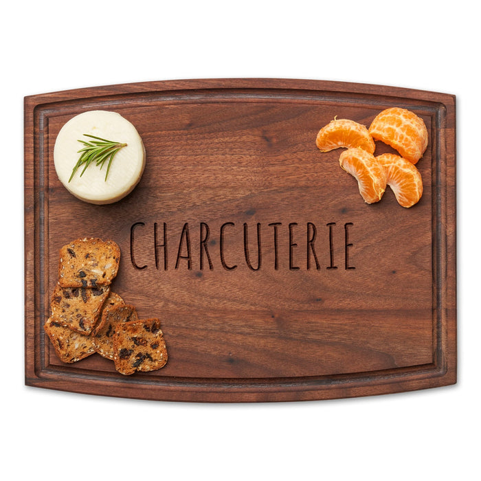 The Maple Arched Artisan Walnut Board | Charcuterie | 12 x 9" features "CHARCUTERIE" text and is topped with a cheese wheel, dried fruit, nut crackers, and peeled mandarin orange segments.