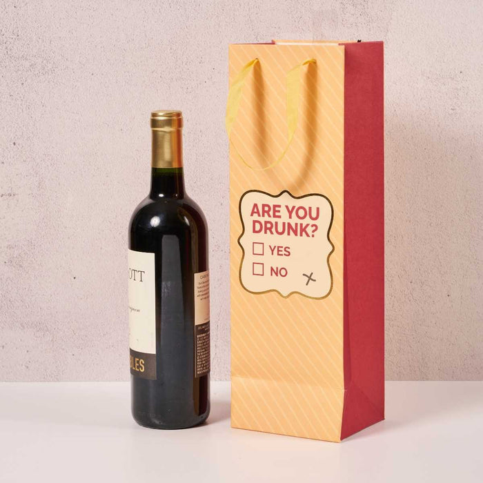 A bottle of wine stands next to the Drinks On Me Are You Drunk- Wine Bag, printed with a checklist reading "ARE YOU DRUNK? YES ☐ NO ☐" and a mark beside NO—a hilarious hostess gift for any occasion.