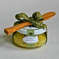 A glass jar of Bella Cucina Artichoke Lemon Pesto Gift Set features a white lid, green ribbon bow, wooden spreader, and a label displaying the product name—an Oprah’s Favorite Things pick.