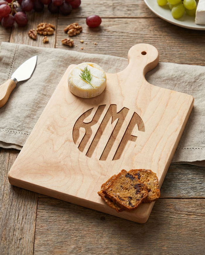 The Maple Artisan Maple Paddle Board | Personalized | 16 x 10" holds brie with dill and fruit & nut bread, set on a rustic table with a cheese knife, grapes, and walnuts.