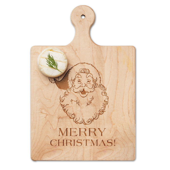 The Maple Artisan Maple Paddle Board | Santa Merry Christmas | 9" x 6" features an engraved Santa above "MERRY CHRISTMAS!" and sits on a white surface with a small round cheese topped with dill placed on its corner.