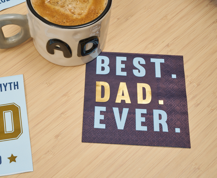 A coffee mug with DAD on it sits beside a card reading BEST. DAD. EVER.—with DAD in gold—on wood, joined by Sugarplum’s Best Dad Ever Cocktail Napkins (26pk) for the perfect Father’s Day tribute.