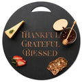 The Maple Black Acacia Round Board (17"x17") features "Thankful Grateful Blessed" engraved in the center—ideal for serving cheese, strawberries, crackers, and honey or as stylish kitchen decor.