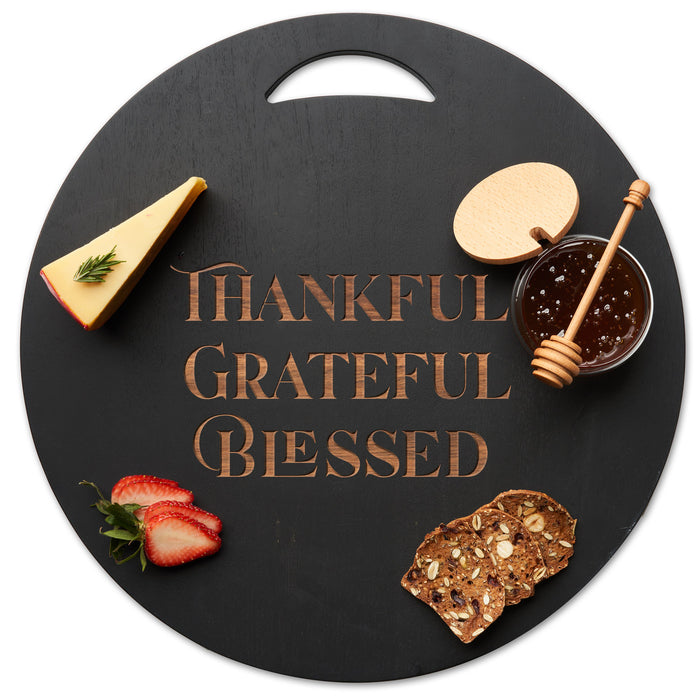 The Maple Black Acacia Round Board (17"x17") features "Thankful Grateful Blessed" engraved in the center—ideal for serving cheese, strawberries, crackers, and honey or as stylish kitchen decor.