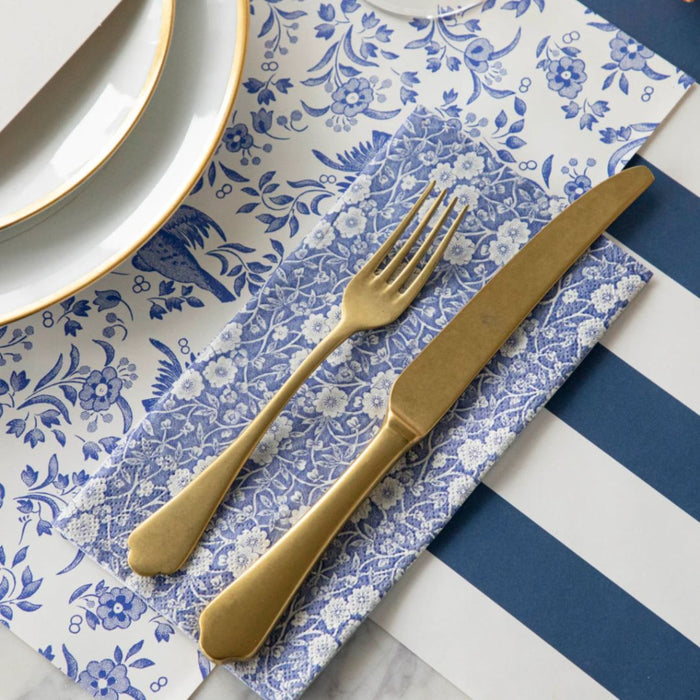 A gold fork and knife rest on elegant table napkins, set atop Hester & Cook Blue Calico Paper Guest Towels beside a white plate with a gold rim.