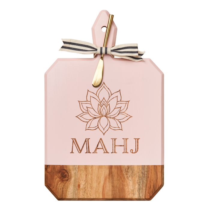 The Maple Acacia Heirloom Board in Blush features a lotus "Mahj" engraving, round handle, and comes with a gold spreader tied with a gray and white ribbon—perfect for your next charcuterie board. Size: 16 x 10".