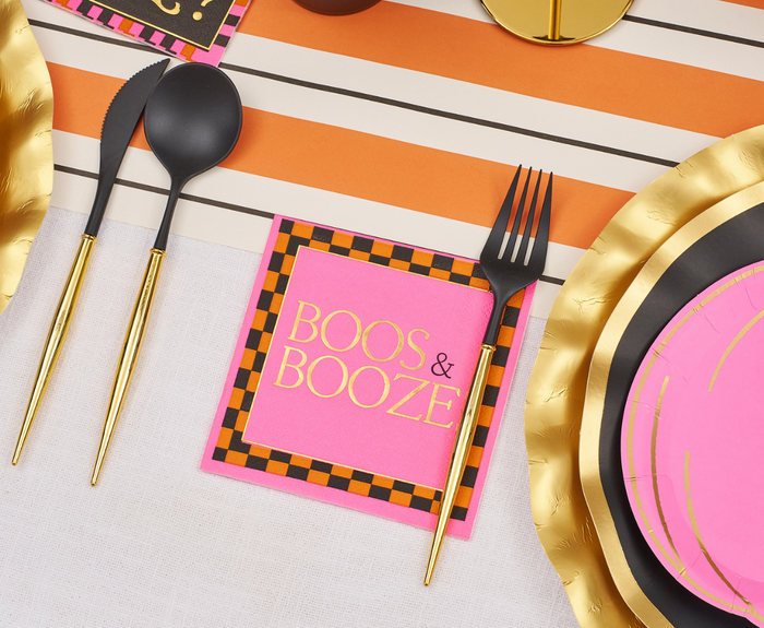 Create a festive Halloween tablescape with black and gold cutlery, gold-rimmed plates, an orange striped runner, and Sugarplum’s Boo Bold Cocktail Napkins (26pk), edged in black-orange checks with “BOOS & BOOZE” in gold lettering.