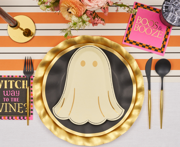 A Halloween table setting features Sugarplum’s Boo Bold Die Cut Salad Plates, black and gold chargers and utensils, a striped orange runner, a floral centerpiece, and napkins reading “BOOS & BOOZE” and “WITCH WAY TO THE WINE?”.