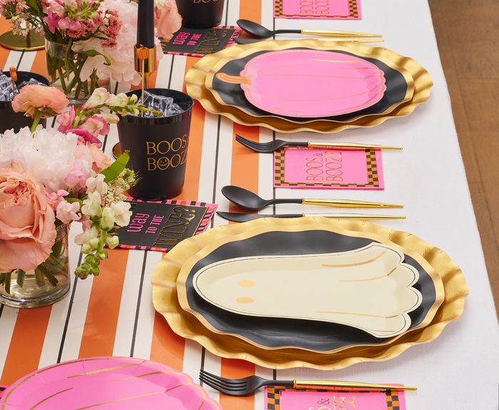 A festive table setting with Sugarplum Boo Bold Die Cut Salad Plates (8pk), black cutlery, pink BOOS & BOOZE napkins, and floral centerpieces for a chic Halloween celebration.