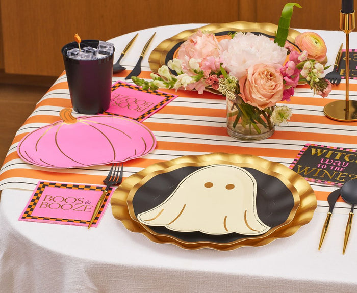 The Sugarplum Boo Bold Table Setting features a striped orange and white runner, ghost-design plates, pink pumpkin plates, a floral centerpiece, black cups, festive napkins, and coordinating Halloween tableware.