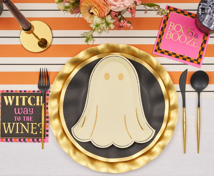 The Sugarplum Boo Bold Table Setting includes ghost-shaped designer paper plates, a black and gold charger, gold cutlery, an orange striped placemat, a floral centerpiece, and cocktail napkins that say BOOS & BOOZE and WITCH WAY TO THE WINE?.