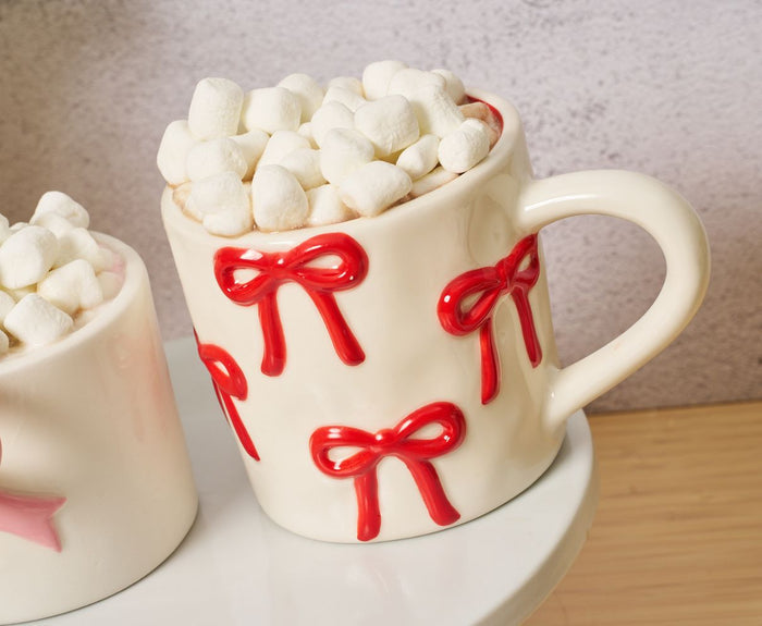 The Sophistiplate LLC Bow Mug + Hot Cocoa Gift Set includes a cream-colored mug with red bows, filled with Bang Candy Hot Cocoa Mix and mini marshmallows—perfect for gifting or enjoying on a cozy day.