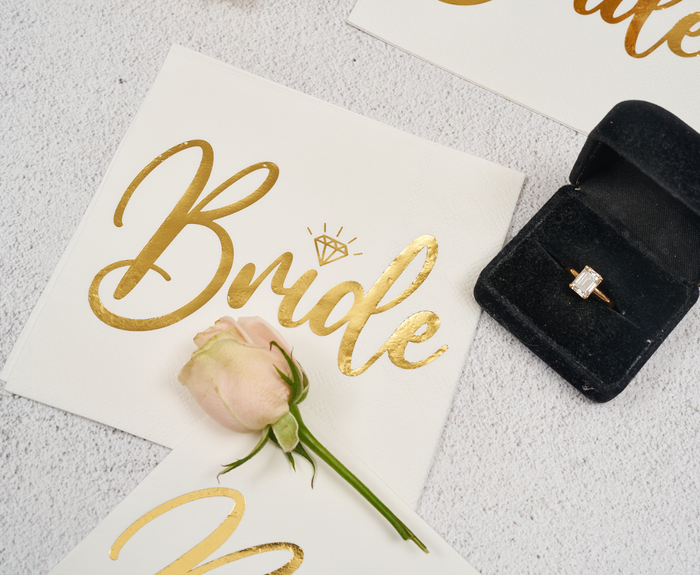Sugarplum Bride Cocktail Napkins (26pk) feature a gold design with a diamond illustration—perfect for adding an elegant touch to bridal showers or bachelorette parties.