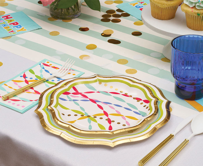 The Sophistiplate Bright Birthday Table Setting features colorful designer disposable plates, a striped runner, gold confetti, cupcakes, a blue glass, gold utensils, and "Happy Birthday" napkins—perfect stylish party tableware.