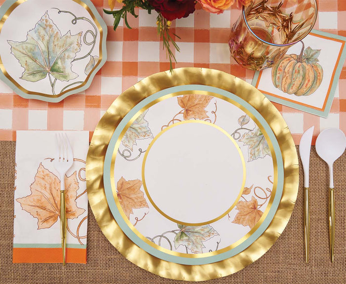 A fall-themed table setting featuring gold-rimmed plates, leaf and pumpkin designs, gold cutlery, a checkered cloth, Sophistiplate Bright & Thankful Appetizer/Dessert Bowls with scalloped edges, and a clear glass with gold details.