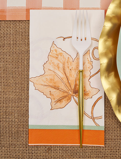 The Sophistiplate Bright & Thankful Guest Towel/20pk features a white napkin with an orange leaf design, styled on burlap. Paired with a gold-rimmed plate and white-gold fork, it adds warm autumn charm to your seasonal gatherings.