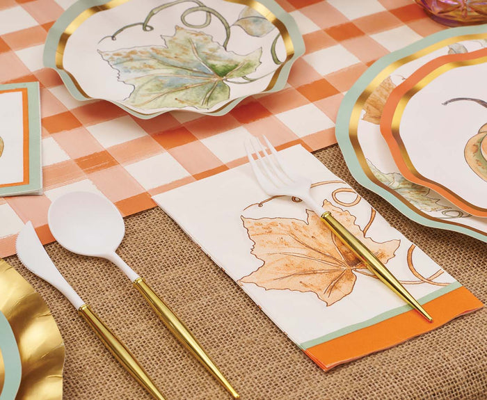 Create a fall-themed table with plates featuring autumn leaves, gold and white cutlery, a checked tablecloth, and Sophistiplate’s Bright & Thankful Guest Towels—perfect for festive gatherings in an orange and white color scheme.