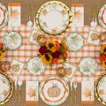 A fall-themed table setting featuring pumpkin and leaf plates, a checkered tablecloth, gold utensils, fall-colored flowers, and autumn leaf napkins is arranged neatly for a festive meal. Bright & Thankful Appetizer/Dessert Bowls by Sophistiplate add a charming touch to the ensemble, perfectly complementing the seasonal décor.