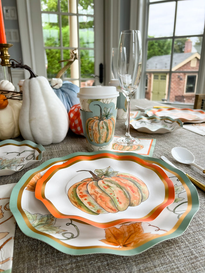 The Bright & Thankful Table Setting by Sophistiplate features designer disposable plates, napkins, and a pumpkin-illustrated cup. Set near a window with pumpkins and leaves as the centerpiece, a champagne flute sits to the right of the plate.