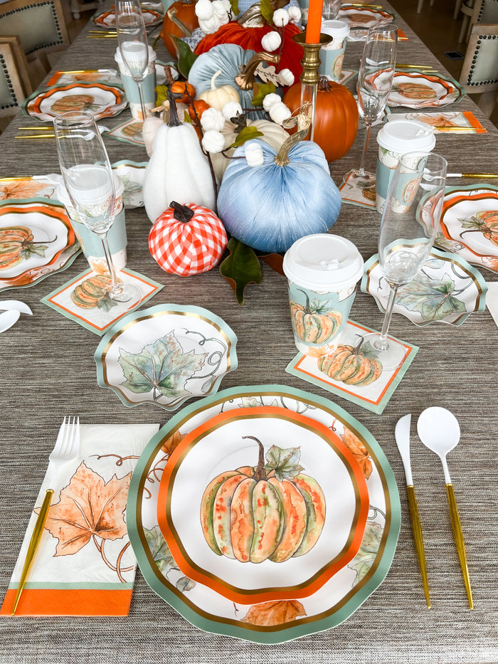 The Bright & Thankful Table Setting by Sophistiplate features autumn-inspired plates, leaf napkins, disposable cups, and orange, white, and blue gourds as a centerpiece for a festive tablescape with coordinated flatware and glasses.
