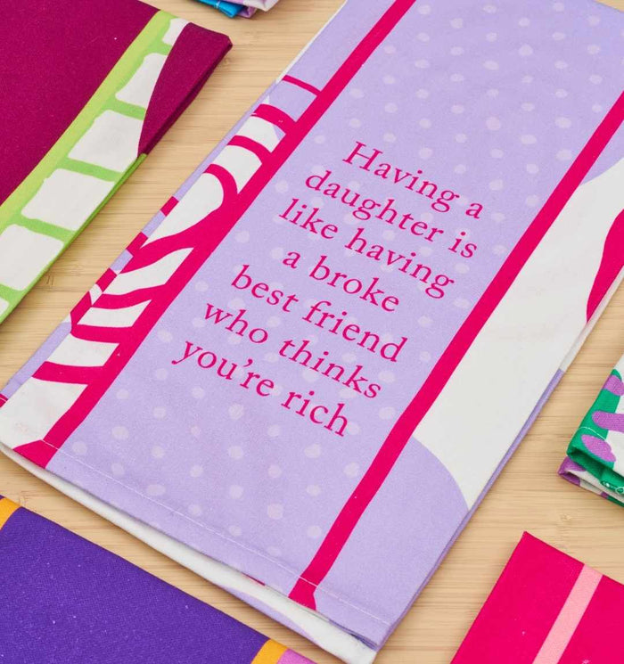 The Broke Best Friend Dish Towel by Drinks On Me is a funny kitchen gift featuring pink and red polka-dot borders and the saying “Having a daughter is like having a broke best friend who thinks you’re rich.”.