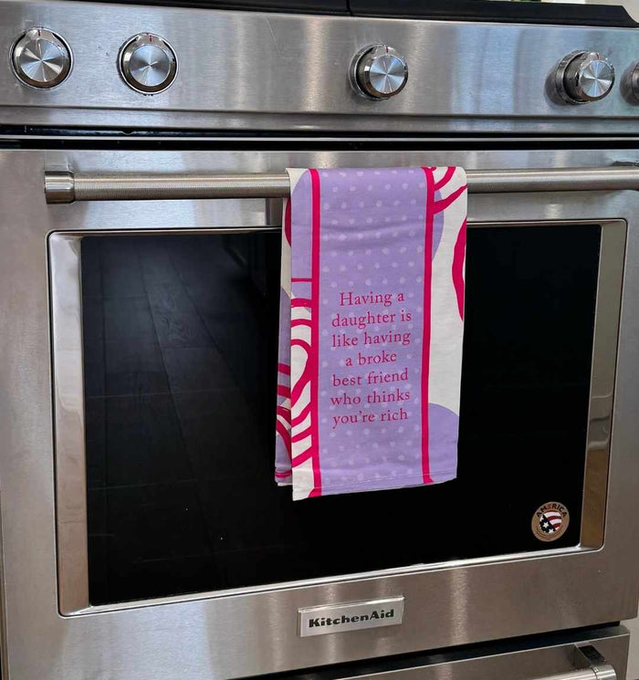 The Broke Best Friend Dish Towel by Drinks On Me adds color and humor to your kitchen with the saying, “Having a daughter is like having a broke best friend who thinks you’re rich.”.