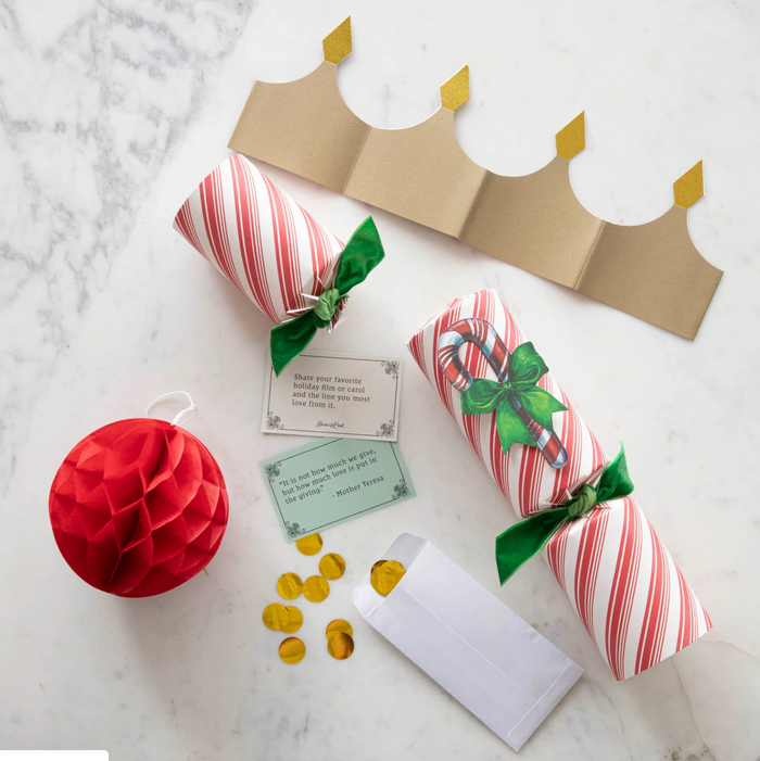The Peppermint Stripe Crackers by Hester & Cook feature red and white stripes and include a gold paper crown, candy cane decoration, gold confetti, joke card, and red honeycomb ornament—perfect festive table decor for your holiday gathering.