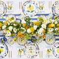 Create a festive table with the Capri Coast Table Setting by Sophistiplate LLC—heavy duty disposable party plates featuring lemon-inspired blue and white patterns, accompanied by white utensils and napkins neatly arranged for effortless and stylish entertaining. A centerpiece of yellow and white flowers completes the vibrant look.