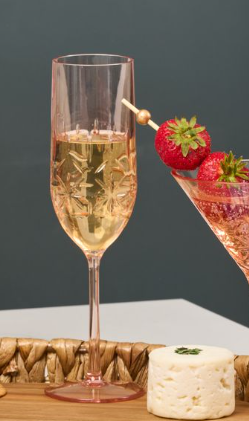 The Sophistiplate Champagne Classic Blush 8.9 Oz flute with an engraved pattern sits next to a martini glass garnished with strawberries and cheese on a wooden tray.