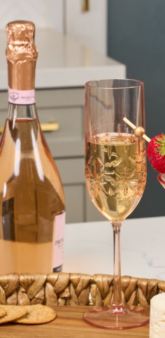 A bottle of Sophistiplate Champagne Classic Blush (8.9 Oz) and a filled shatterproof flute with a strawberry skewer garnish sit on a tray with crackers.