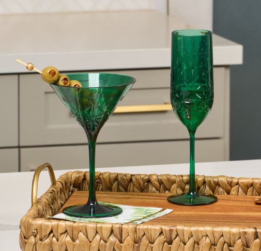 A Green Champagne Classic 8.9 Oz by Sophistiplate and a martini glass with olives rest on a woven tray atop the kitchen counter.