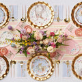 Create a festive look with the Sophistiplate Charming Easter Table Setting, featuring bunny and chick plates, gold cutlery, pink and purple glassware, striped napkins, plus a floral centerpiece with eggs and greenery.