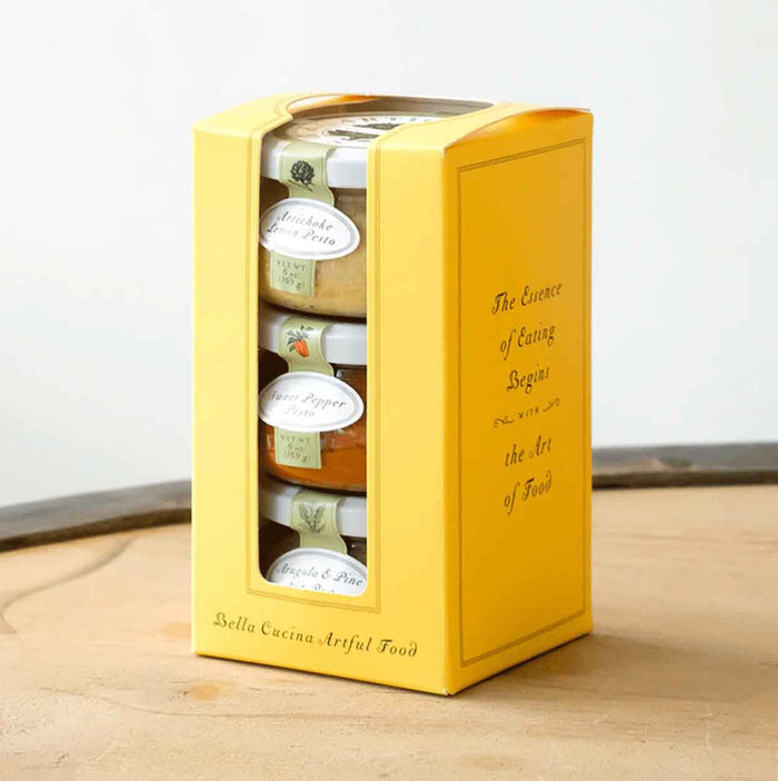 A yellow box labeled "Chef’s Selection Pesto Set" by Bella Cucina holds three jars of gourmet pesto and spreads—each a different flavor. The perfect addition to any charcuterie board or appetizer spread.