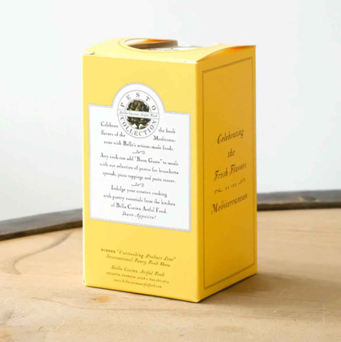 A yellow rectangular box with white and black text and a circular logo near the top, the Bella Cucina Chef’s Selection Pesto Set stands upright on a light surface—a perfect gift idea against a neutral background.