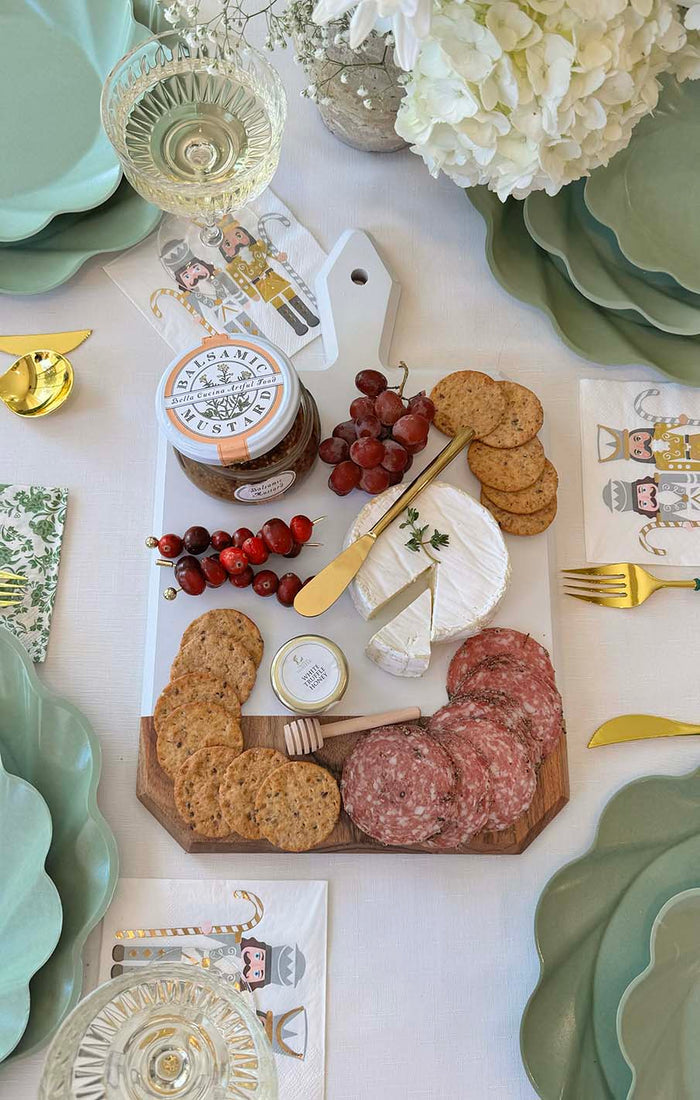 The Sophistiplate Christmas Board Gift Kit: Gilded Nutcracker features an acacia wood charcuterie board with crackers, salami, brie, grapes, cranberries, fig spread, and gold utensils—an elegant hostess gift for any holiday table.