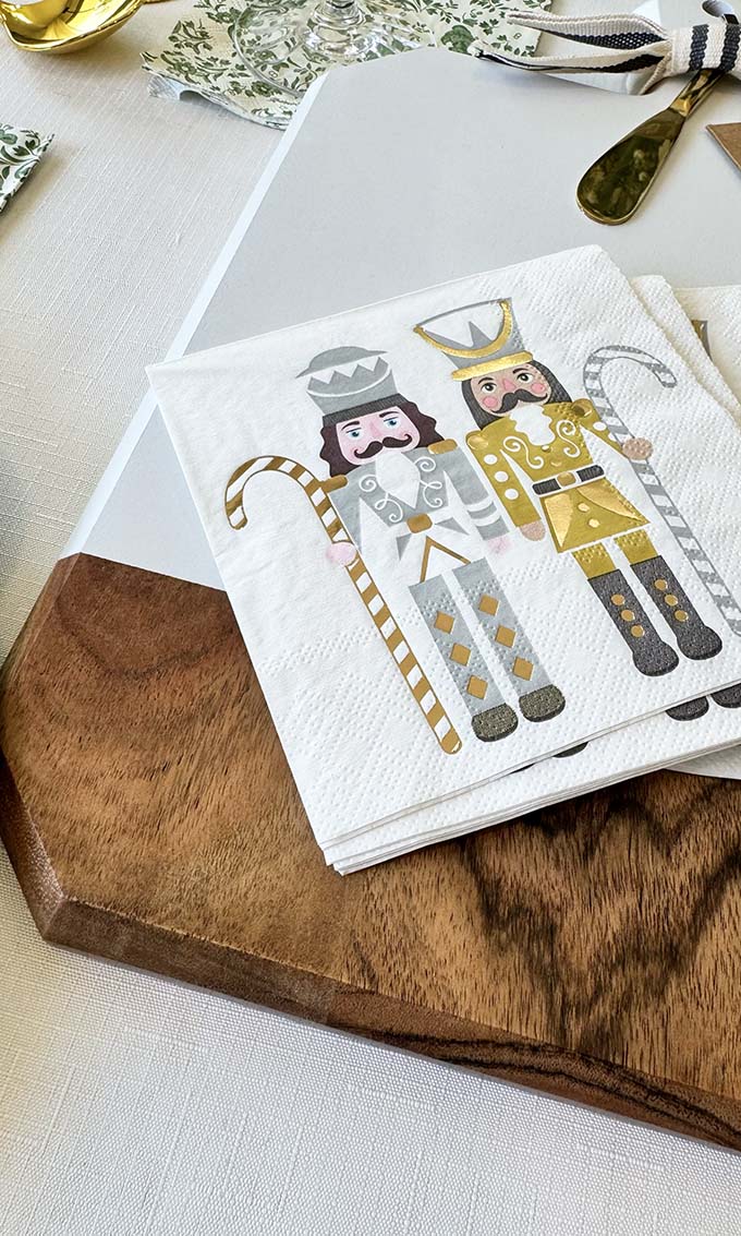 The Sophistiplate Christmas Board Gift Kit: Gilded Nutcracker includes napkins with nutcracker designs and an acacia wood serving board—an ideal festive hostess gift for your dining table.