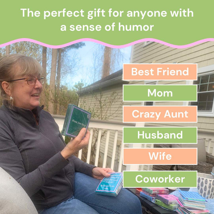 A smiling woman with glasses sits on a porch holding a Drinks On Me Christmas Coaster Bundle—Version 1. The perfect funny Christmas gift or stocking stuffer for your best friend, mom, crazy aunt, husband, wife, or coworker.