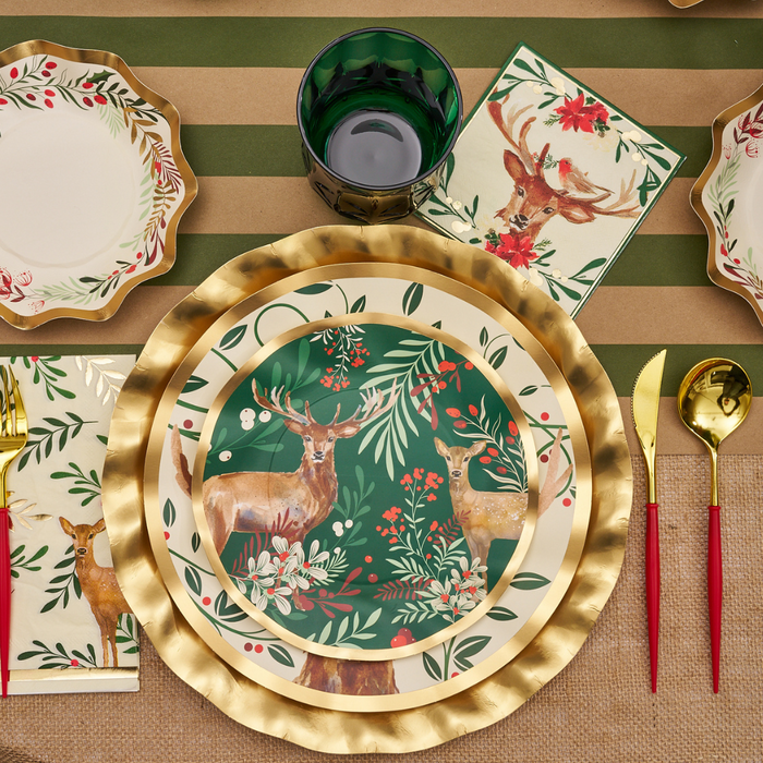 Table setting with Sophistiplate Christmas Forest Salad Plates (8 pack), gold charger, green glass, gold cutlery with red handles, and napkins on a brown and green striped tablecloth.
