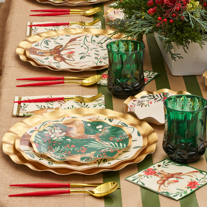 Holiday table setting featuring gold-rimmed reindeer salad plates from the Christmas Forest Salad Plates/8pk by Sophistiplate, paired with red-handled gold cutlery, green glass tumblers, floral napkins, and a festive centerpiece of berries and greenery.
