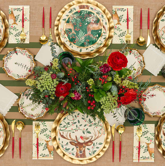 Create a festive holiday table with the Sophistiplate Christmas Forest Table Setting, featuring gold flatware, red candles, a floral centerpiece, and deer-and-botanical plates. Striped runner and themed napkins complete this elegant arrangement.