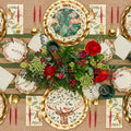 Create a festive holiday table with the Sophistiplate Christmas Forest Table Setting, featuring gold flatware, red candles, a floral centerpiece, and deer-and-botanical plates. Striped runner and themed napkins complete this elegant arrangement.