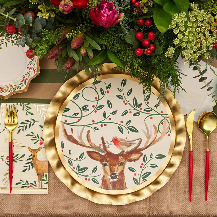 The Sophistiplate Christmas Forest Table Setting features festive disposable plates with a painted deer, red berries, and bird, along with gold cutlery with red handles and matching deer napkins for charming holiday party décor.