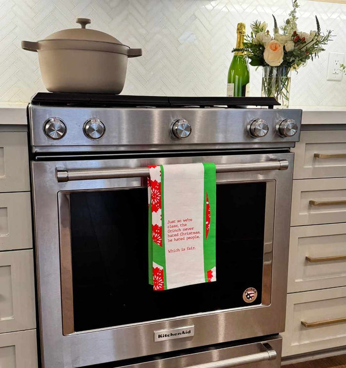 A bright kitchen features a stainless steel oven with the CHRISTMAS Grinch Dish Towel by Drinks On Me hanging on the handle—perfect for gifting to friends who love to cook.