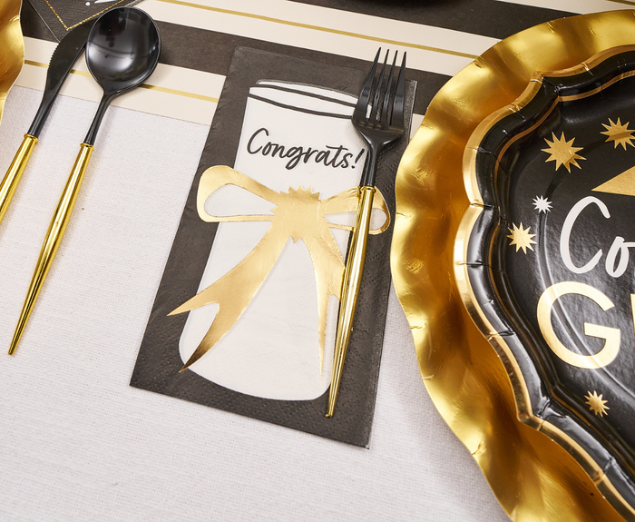 The Sophistiplate Classic Grad Table Setting features black napkins with gold bows and "Congrats!" under black cutlery, plus “Congrats Grad” designer plates—perfect for elevating your graduation party supplies.
