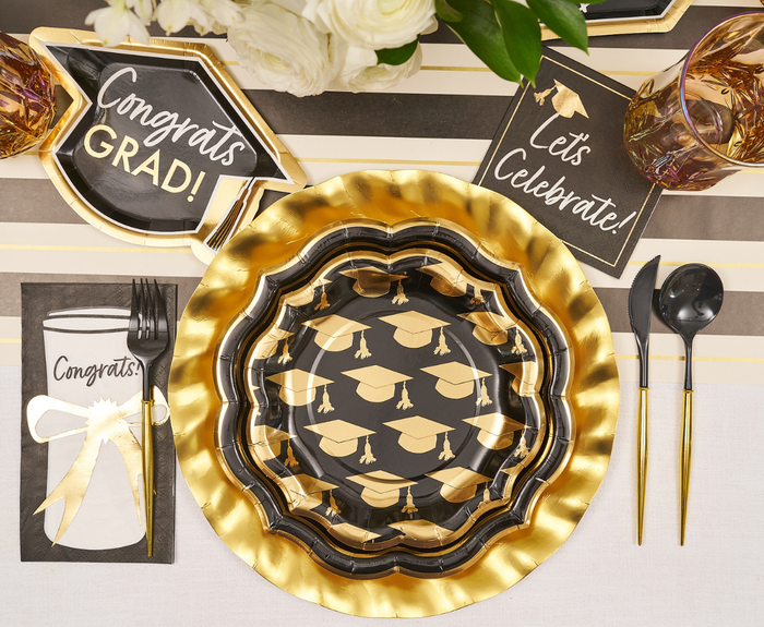Celebrate graduation with a festive table set using Sophistiplate's Classic Grad Salad Plates (8pk), featuring graduation cap designs, paired with gold utensils, celebratory napkins, and a white flower centerpiece.