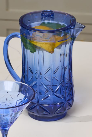 The Sophistiplate Classic Pitcher | Cobalt | 53 Oz, BPA-free and filled with water, lemon slices, and mint leaves, rests on a white surface with a matching cobalt glass partly visible in the foreground.